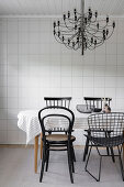 Dining area with various chairs and chandeliers in front of a tiled wall