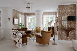 Antique upholstered furniture and a Swedish tiled stove in a living room with floral wallpaper