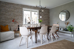 An antique wooden table with modern chairs in a dining room with papered walls