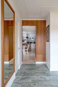 A hallway with a large wall mirror, teak panelling and a tiled floor