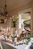 Festively set Christmas table with lily and mercury candlesticks, above antique copper chandelier