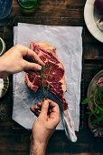 Hände marinieren rohes Tomahawk-Steak mit Kräutern