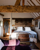 Antique suitcases and Victorian chaise longue in bedroom with wooden beams.