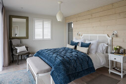 Blue quilt on double bed with wood cladding in coastal home