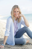 A blonde woman by the sea wearing a purple t-shirt and a blue-and-white striped shirt