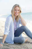 A blonde woman by the sea wearing a blue-and-white striped shirt and jeans