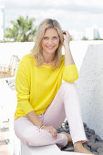 A blonde woman wearing a yellow jumper and white trousers