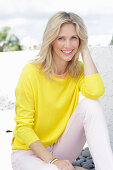A blonde woman wearing a yellow jumper and white trousers