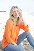 Blonde Frau in orangefarbener Tunikabluse und Jeans am Meer