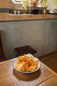 Pile of crispy potato chips in bowl placed on wooden table at home