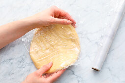Flattened pastry being wrapped in plastic and chilled