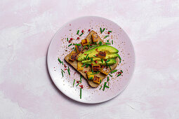 Homemade toasted bread from above with avocado, mango and aromatic herbs on pink background