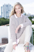 A young blonde woman on the beach wearing a light jumper and trousers