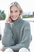 A young blonde woman on the beach wearing a grey knitted jumper