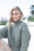 A young blonde woman on the beach wearing a grey knitted jumper
