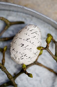 Mit beschriebenem Stoff beklebtes Ei zwischen Zweigen mit Knospen