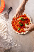 Pizza zubereiten, mit Basilikumblättern bestreuen