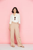A brunette woman wearing a white blouse and pink Marlene trousers