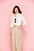 A brunette woman wearing a white blouse and pink Marlene trousers