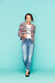 A dark-haired woman wearing a t-shirt, a striped jacket and jeans