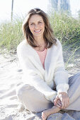 Langhaarige Frau in hellem Pullover und Hose im Sand am Strand