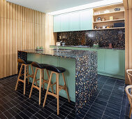 Kücheninsel mit schwarzem Terrazzo und grünen Fronten in offener Küche