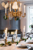 Table festively set for Christmas below candle chandelier with grey sideboard in background