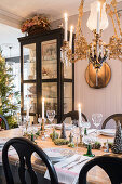 Table festively set for Christmas below candle chandelier with display cabinet in background