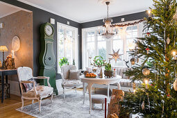 Round table below crystal chandelier, seating, longcase clock and Christmas tree with lights in lounge