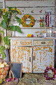 A harvest still life with apples, red onions, an autumn wreath and sunflowers near an old kitchen cupboard