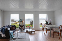 Sofa, coffee table and dining area in room with white-painted wood panelling