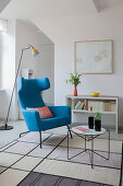 Blue wing-back chair, standard lamp and coffee table in open-plan interior