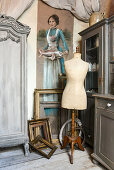 Tailors' dummy and gilt picture frames below portrait of woman holding a fish