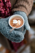 Gloved hands holding hot chocolate with marshmallow