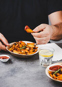 Man eating fried potato wedges with barbecue sauce