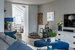 View across sofa to blue ottoman used as coffee table and white chest of drawers