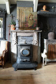 Old stove in front of fireplace with religious painting on mantelpiece and vintage-style accessories