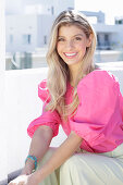 A young blonde woman wearing a pink top with puffed sleeves and white summer trousers