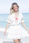 A young blonde woman wearing a white embroidered summer dress