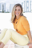 A young blonde woman wearing an orange cardigan and a pair of light trousers
