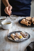 Sprinkling filled cannoli with powdered sugar