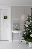 Christmas tree and console table with mirror against patterned wallpaper