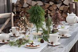 Kleine Bäumchen für weihnachtliche Tischdekoration basteln: gedeckter Tisch mit gebundenen Bäumchen aus Kiefer, Ahorn und Haselzweigen