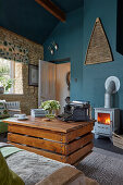 DIY coffee table made from reclaimed wood on castors and wood-burning stove in living room with petrol-blue wall