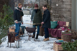 Friends standing comfortably around firepit and toasting stick bread