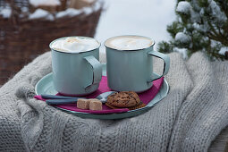 Tassen mit heißem Cappuccino auf Teller mit Zucker, Keks und Kaffeelöffeln