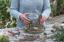 votive surrounded by twigs: Woman dresses up canning jar with twigs and bark