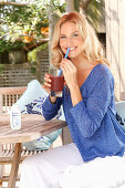 A blonde woman wearing a blue shirt and white trousers with a drink