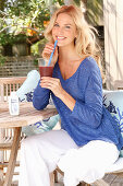 A blonde woman wearing a blue shirt and white trousers with a drink