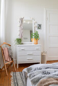 White chest of drawers with a mirror and clothes rack in a corner of the bedroom